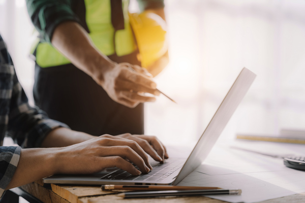 two professionals collaborating on laptop with construction tools nearby