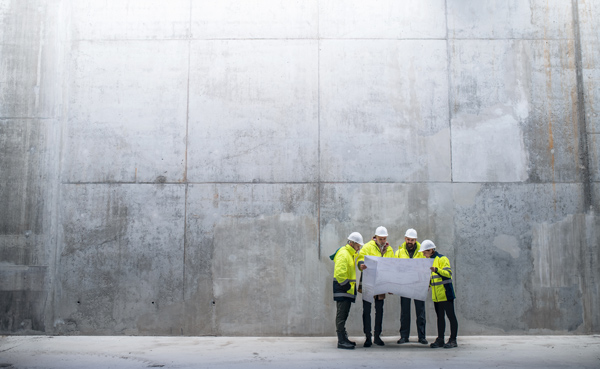 group of construction workers discussing blueprints in a large industrial space with concrete walls focused on planning two projects