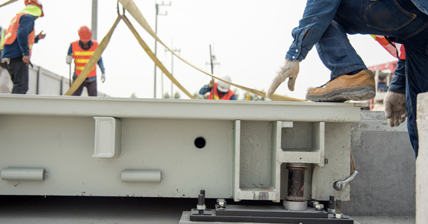 construction workers using a hoisting system to install a heavy panel on a building project including safety gear and tools related to infrastructure development and 11 installation techniques