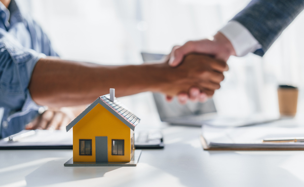 miniature yellow house with two people shaking hands in a business setting representing real estate transactions and agreements for new homeowners or investors