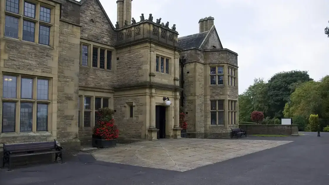 Haworth Art Gallery's stone gabled façade and tall chimney stacks amid shrubs and lawn in Accrington.