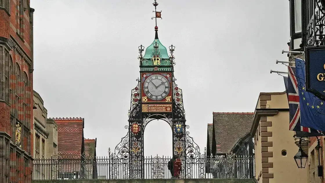The ornate red-and-gold Eastgate Clock above a sandstone arch spanning a pedestrian street in Chester.