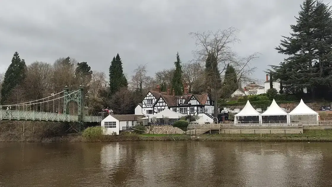 The River Severn curving past riverside buildings and a church spire in Shrewsbury.