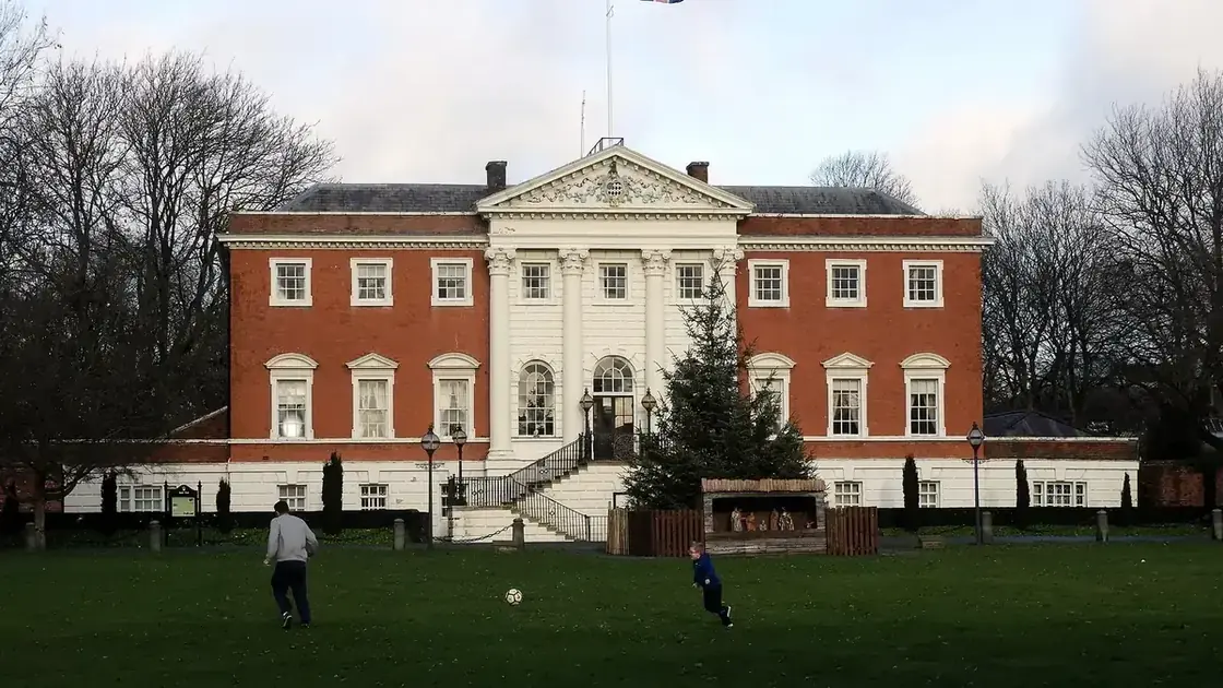 Warrington Town Hall's pale stone façade seen across its lawn and gardens, framed by bare trees.